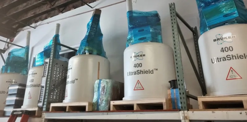 White Bruker UltraShield 400 NMR machines are lined up on shelves, wrapped with blue protective material, in an industrial setting.