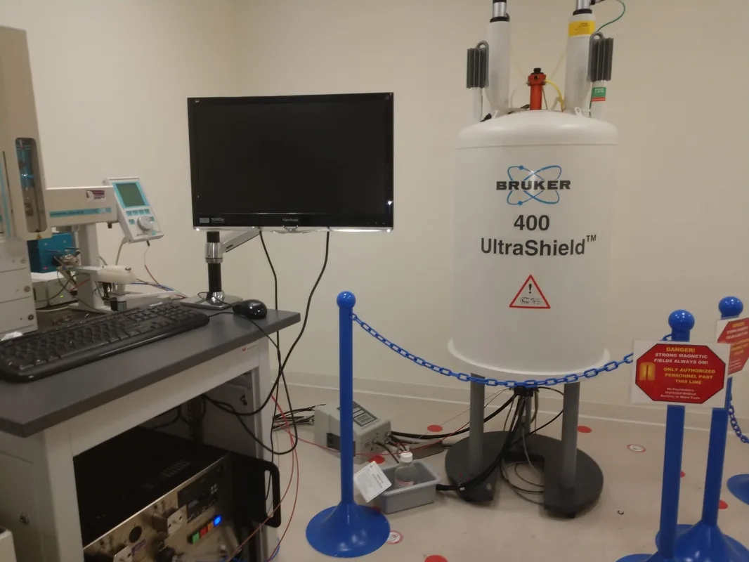 Laboratory with a Bruker 400 UltraShield NMR machine, a computer setup, and safety signs around the equipment.